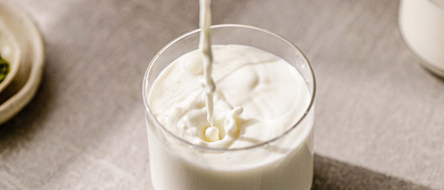 milk being poured into an almost full glass of milk